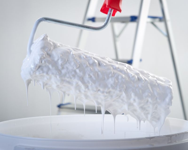 Ein Farbroller wird aus einem Eimer weißer Farbe rausgeholt